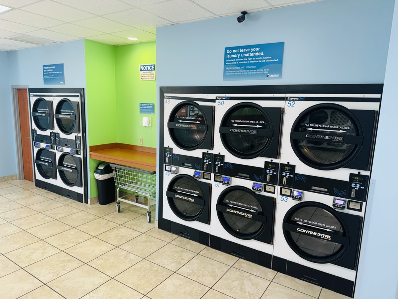 Stacked dryers beside a folding table and rolling laundry cart